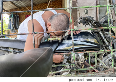 A man repairs an old motorcycle with a sidecar A man repairs an old motorcycle with a sidecar 132915726