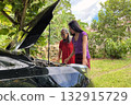 An elderly and young Asian woman looks under the hood of a broken down car to find a problem with the engine 132915729