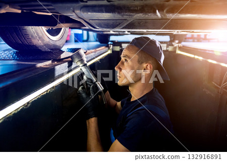 Car mechanic examining car suspension of lifted automobile at service station Car mechanic examining car suspension of lifted automobile at service station 132916891