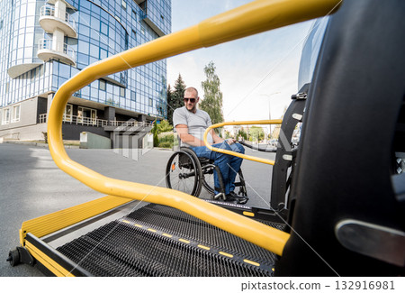 A man in a wheelchair moves to the lift of a specialized vehicle A man in a wheelchair moves to the lift of a specialized vehicle 132916981