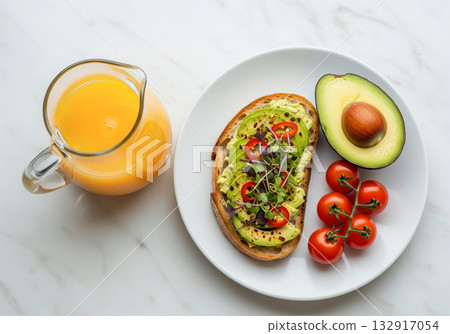 Vibrant Morning Fuel: Healthy Avocado Toast, Cherry Tomatoes, and Fresh Orange Juice Served on White Marble. 132917054