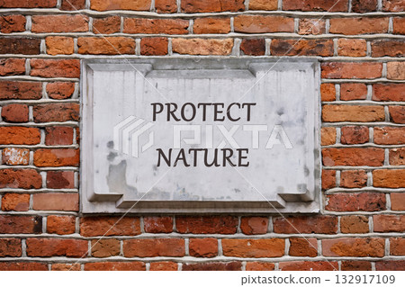 A weathered sign on a brick wall boldly declares the message to protect nature. This reminder highlights our responsibility to care for the earth and its resources A weathered sign on a brick wall boldly declares the message to protect nature. This reminder highlights our responsibility to care for the earth and its resources 132917109