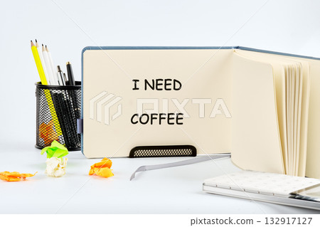 A cozy workspace features a notepad open to the phrase I need coffee. Colorful pens and crumpled paper add a playful touch, inviting creativity and focus for the day ahead 132917127