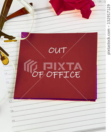 A bold sticky note states out of office on a tidy desk. Nearby glasses rest among neatly arranged notes and a delicate rose, suggesting a moment of peace and time away from work 132917129