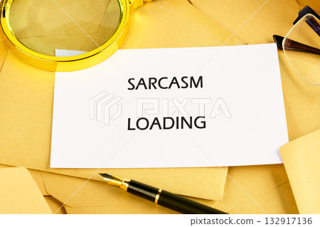 A humorous message on a card stating sarcasm loading is placed on a cluttered desk filled with envelopes, a magnifying glass, and a stylish pen, reflecting a playful office atmosphere 132917136