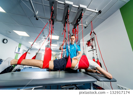 Physiotherapy. Suspension training therapy. Young man doing fitness traction Physiotherapy. Suspension training therapy. Young man doing fitness traction 132917174