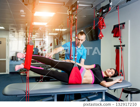 Physiotherapy. Suspension training therapy. Young woman doing fitness traction 132917210
