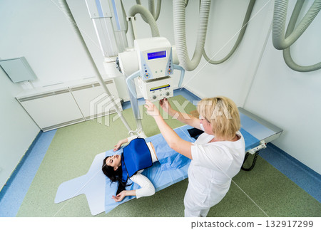Radiologist and patient in a x-ray room. Classic ceiling-mounted x-ray system. 132917299
