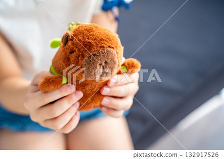 A plush capybara toy held in a child hands. The image reflects Gen Z love for internet-inspired mascots and the aesthetic comfort culture of soft toys. 132917526