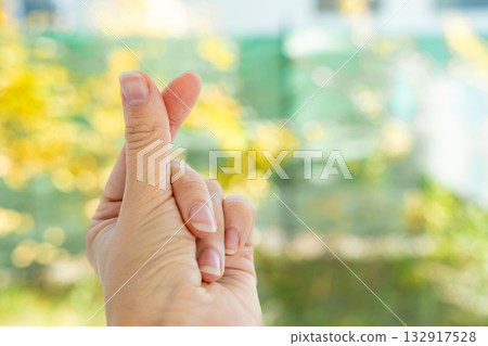 Teenage hand making finger heart gesture outdoors with blurred nature background. Young generations showing love, positivity and Gen Z pop culture trend. Teenage hand making finger heart gesture outdoors with blurred nature background. Young generations showing love, positivity and Gen Z pop culture trend. 132917528