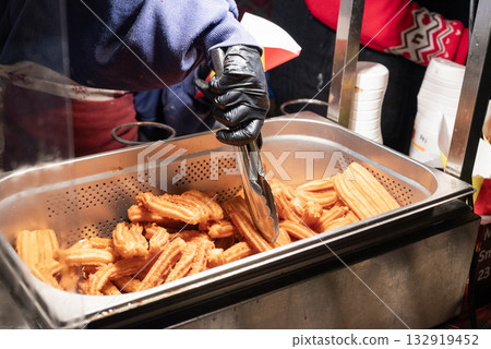 preparing fried sweet churros street food in the city center at the Christmas market in Krakow, Poland. preparing fried sweet churros street food in the city center at the Christmas market in Krakow, Poland. 132919452