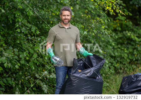 Eco volunteer. Garbage collecting in forest. Eco-friendly waste solutions. Volunteer collecting garbage, ecology. Man in rubber gloves with trash bag clean up garbage. Man collecting plastic trash 132919732