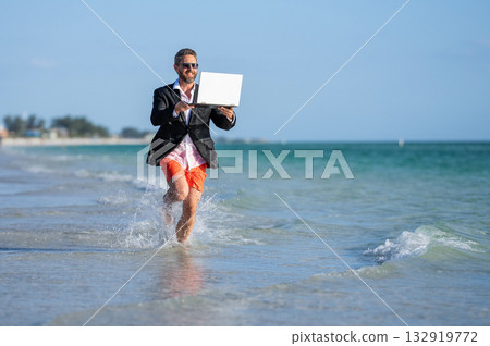 Business man in suit running with laptop at sea. successful business man enjoy summer. business man on summer vacation. business success of man. Beach meetings and conferences Business man in suit running with laptop at sea. successful business man enjoy summer. business man on summer vacation. business success of man. Beach meetings and conferences 132919772