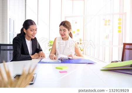 Two young Asian businesswoman in smart casuals read some documents, making plans together. Business people talking together with documents at office. Two young Asian businesswoman in smart casuals read some documents, making plans together. Business people talking together with documents at office. 132919929