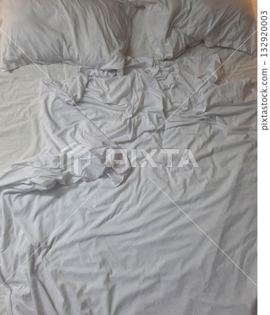 Soft white bedding with rumpled sheets and pillows creating a cozy and inviting atmosphere Soft white bedding with rumpled sheets and pillows creating a cozy and inviting atmosphere 132920003