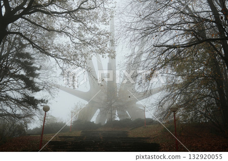 Mysterious view of the Kosmaj Monument rising through dense fog, surrounded by autumn trees and quiet forest atmosphere Mysterious view of the Kosmaj Monument rising through dense fog, surrounded by autumn trees and quiet forest atmosphere 132920055