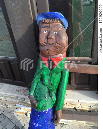 Funny wooden sculpture of smiling man with green jacket and blue hat. Folk tradition, handmade artistry, and human creativity. Funny wooden sculpture of smiling man with green jacket and blue hat. Folk tradition, handmade artistry, and human creativity. 132920093