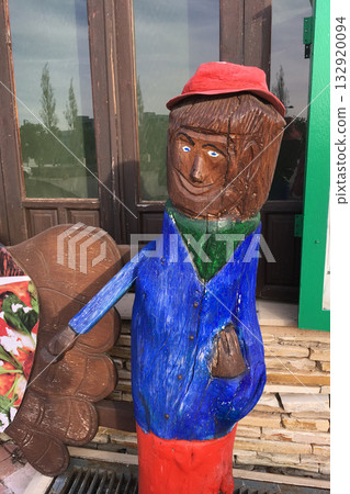 Colorful wooden funny sculpture of man figure near door. Folk art, craftsmanship, and cultural creativity in local expression. Colorful wooden funny sculpture of man figure near door. Folk art, craftsmanship, and cultural creativity in local expression. 132920094
