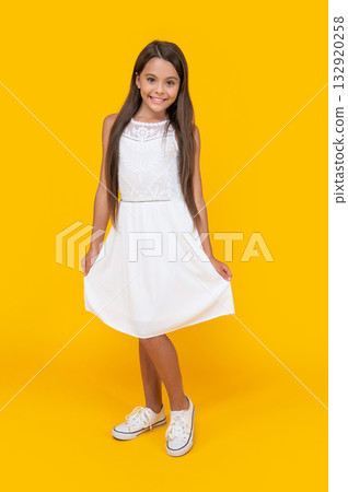 adorable teen girl in white dress standing on yellow background 132920258
