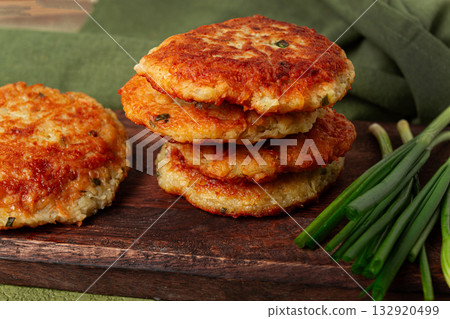 Crispy potato pancakes Latkes, stacked on a wooden board next to fresh green onions, natural light, homemade, no people, Crispy potato pancakes Latkes, stacked on a wooden board next to fresh green onions, natural light, homemade, no people, 132920499