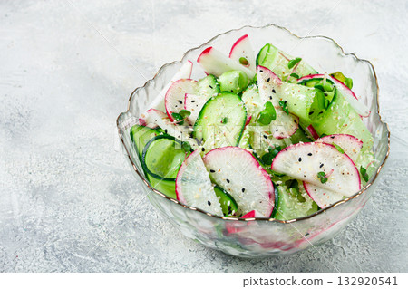 Fresh cucumber and radish salad served in a clear bowl with herbs on a light textured surface 132920541