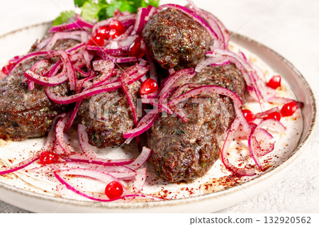 grilled kebabs topped with onions and pomegranate on a white plate in a bright kitchen setting 132920562