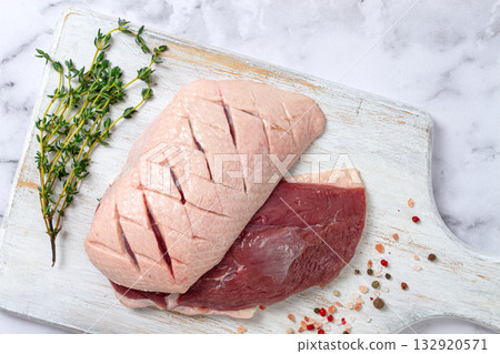 Fresh raw duck breasts, spread on a wooden cutting board, with herbs and spices, on a white marble surface Fresh raw duck breasts, spread on a wooden cutting board, with herbs and spices, on a white marble surface 132920571