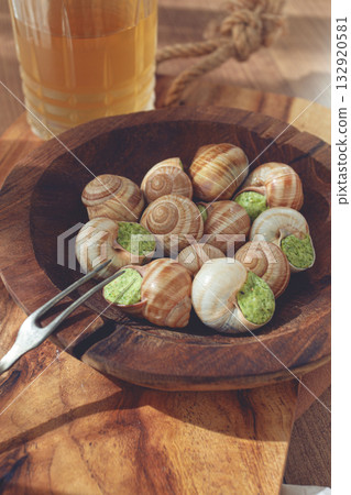 Snails cooked with herb oil on a wooden plate, served with white wine, natural light, no people, 132920581
