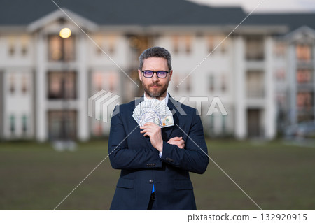 Successful realtor in suit with money dollar. House owner hold money outdoor. Realtor offering new home. Broker make offer. Businessman broker with money. Property concept. Licensed real estate agent Successful realtor in suit with money dollar. House owner hold money outdoor. Realtor offering new home. Broker make offer. Businessman broker with money. Property concept. Licensed real estate agent 132920915