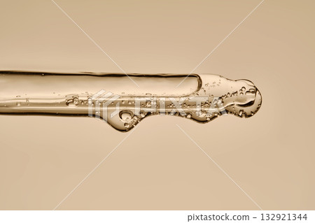The texture of the serum flowing out of the pipette on a beige background. The texture of the serum flowing out of the pipette on a beige background. 132921344