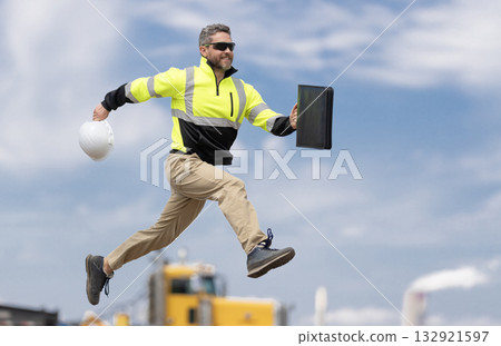 Man engineer running to success. Builder man run fast to work. Engineer supervisor running outdoor. Supervisor jumping. Excited builder construction worker jumping in front of trucks. Good job Man engineer running to success. Builder man run fast to work. Engineer supervisor running outdoor. Supervisor jumping. Excited builder construction worker jumping in front of trucks. Good job 132921597