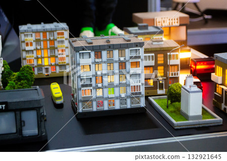 Prototype building printed on 3D printer from melted plastic. 3D-printed building prototype. A house created on 3D printer with gray walls, gray roof, and illuminated windows and balconies. Prototype building printed on 3D printer from melted plastic. 3D-printed building prototype. A house created on 3D printer with gray walls, gray roof, and illuminated windows and balconies. 132921645