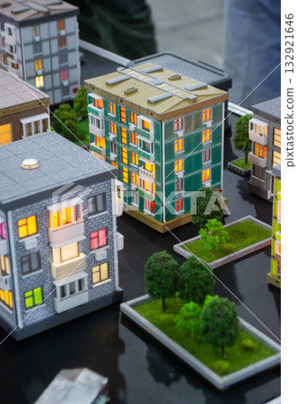 Prototype building printed on 3D printer from melted plastic. 3D-printed building prototype. A house created on 3D printer with green walls, gray roof, and illuminated windows and balconies. 132921646