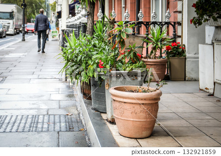 Decorative potted plants and flowers placed along a city sidewalk beside a building 132921859