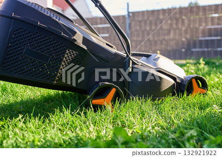 Electric lawn mower cutting green grass in backyard Electric lawn mower cutting green grass in backyard 132921922