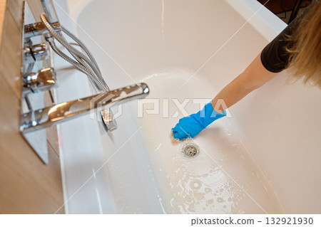 Hand in rubber glove cleaning bathtub with sponge and soap foam 132921930