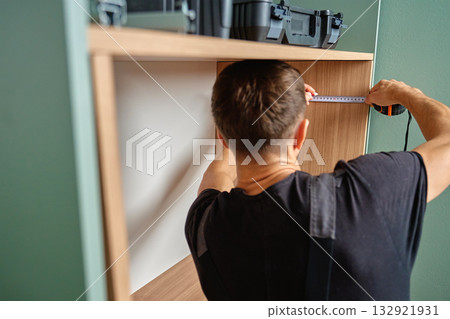 Worker measuring and marking wooden cabinet during furniture assembly 132921931