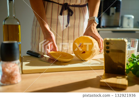 Woman slicing pumpkin on cutting board in kitchen Woman slicing pumpkin on cutting board in kitchen 132921936