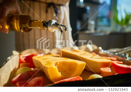 Woman pouring olive oil over pumpkin and vegetables in kitchen 132921943