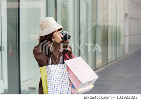 Asian woman enjoys mall shopping, fashion lifestyle, holding bags outside, taking photograph with camera, great for people and buyer promotions. 132922022