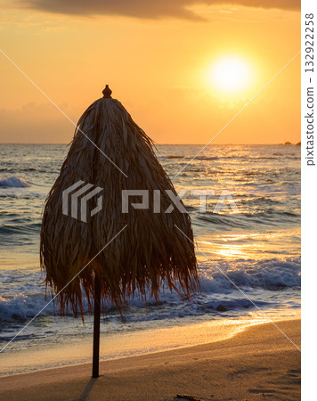 umbrella on the sand beach at sunrise. summer vacation at the sea. blue sky with glowing clouds. beautiful landscape for travel with sun above horizon. tranquil scenery in orange light umbrella on the sand beach at sunrise. summer vacation at the sea. blue sky with glowing clouds. beautiful landscape for travel with sun above horizon. tranquil scenery in orange light 132922258