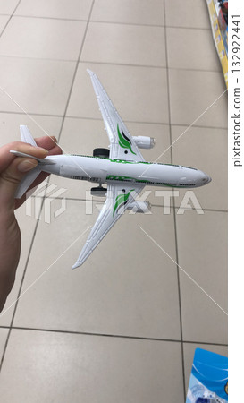 A hand holding a white toy airplane with green accents. Representation of childhood imagination, aviation fascination, and dreams of global travel. A hand holding a white toy airplane with green accents. Representation of childhood imagination, aviation fascination, and dreams of global travel. 132922441