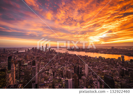 Aerial view of New York City at sunset with vibrant orange sky reflecting in the Hudson River and illuminated skyscrapers under dramatic clouds 132922460