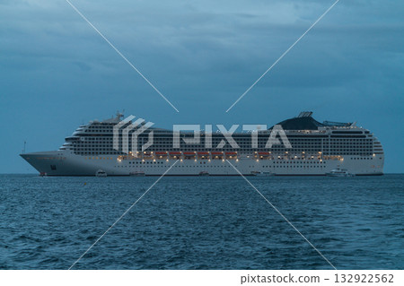 A large modern cruise ship at sea at dusk, side view. Illuminated decks, lifeboats, numerous windows and balconies A large modern cruise ship at sea at dusk, side view. Illuminated decks, lifeboats, numerous windows and balconies 132922562