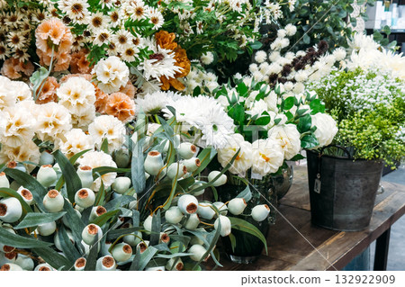 Assorted white and pastel faux florals including roses, daisies, and lotus pods in display. Budget-friendly decor for hospitality and retail, faux flowers for restaurants, cost-effective design 132922909