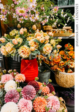 Colorful arrangement of artificial roses, dahlias, and cosmos in vases and baskets across a display shelf. Artificial florals, reusable bouquets, sustainable interiors, decor longevity Colorful arrangement of artificial roses, dahlias, and cosmos in vases and baskets across a display shelf. Artificial florals, reusable bouquets, sustainable interiors, decor longevity 132922923