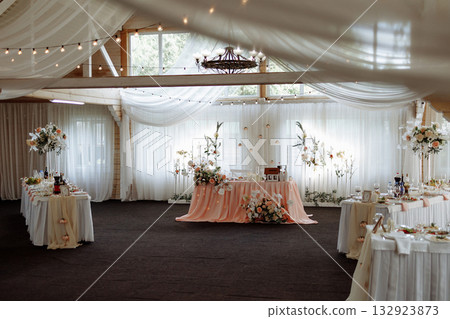 Elegant wedding banquet hall with floral decor and white drapery under wooden ceiling Elegant wedding banquet hall with floral decor and white drapery under wooden ceiling 132923873
