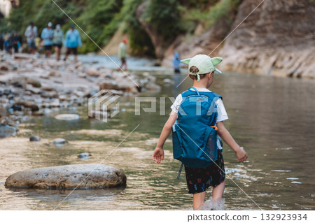 Young child with a backpack and hat hiking the Narrows of Zion National Park along the Virgin River at midday 132923934