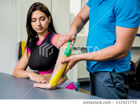 Kinesiotaping. Physical therapist applying tape to young beautiful womans spine Kinesiotaping. Physical therapist applying tape to young beautiful womans spine 132925770