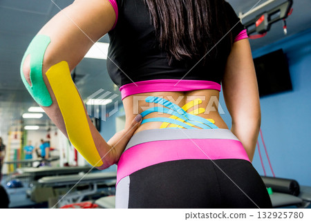 Kinesiotaping. Physical therapist applying tape to young beautiful womans spine Kinesiotaping. Physical therapist applying tape to young beautiful womans spine 132925780